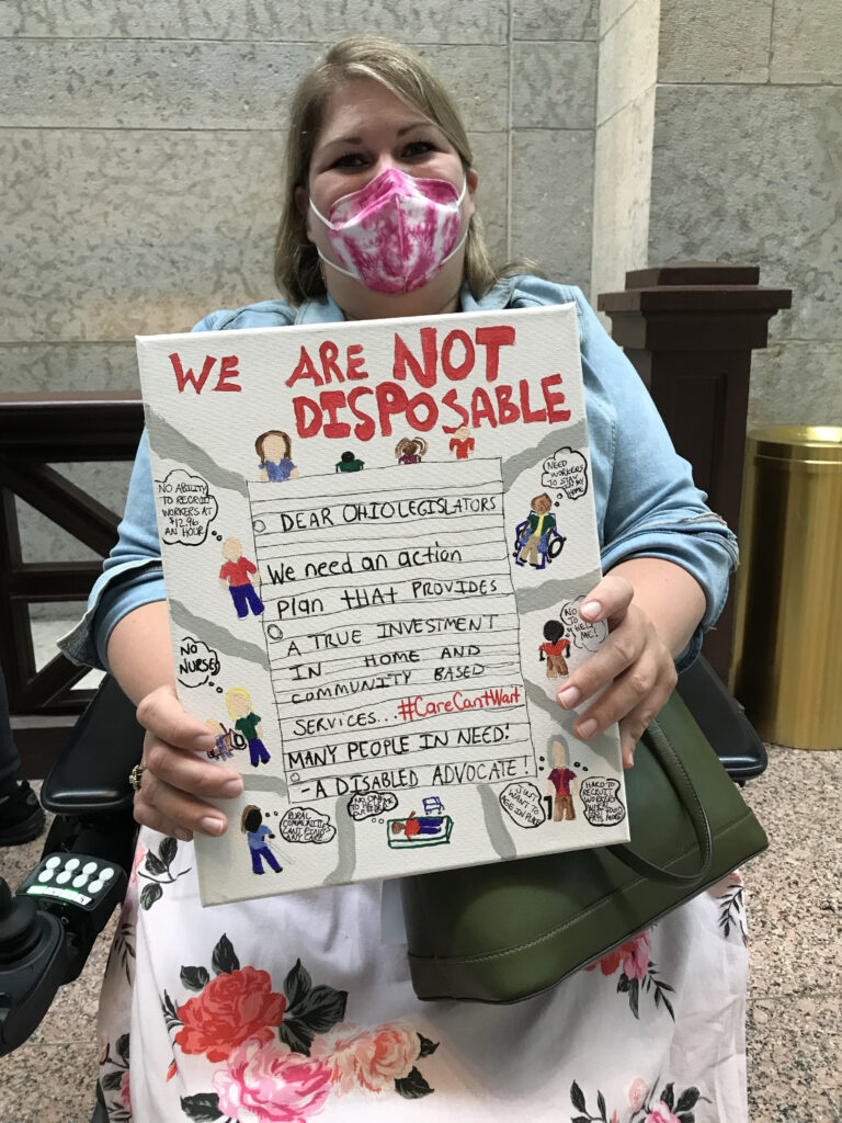 Katie Shelley holding a hand-painted sign with the statement, "We are not disposable."